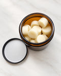 Open amber jar of Daily Dots, small round tallow lotion bar dots, with the lid set beside it