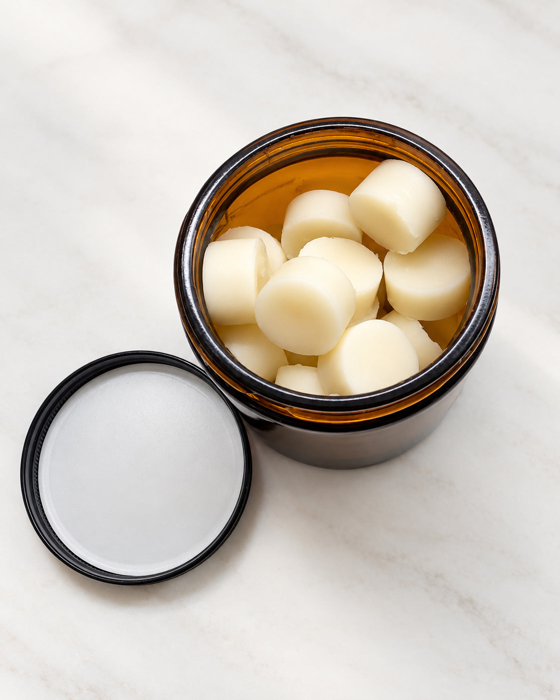 Open amber jar of Daily Dots, small round tallow lotion bar dots, with the lid set beside it